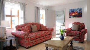 Un soggiorno con un divano rosso dal motivo decorativo, una poltrona coordinata, un tavolino in legno e un quadro appeso al muro.