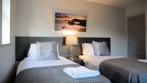 Una camera d'hotel con due letti, un comodino con una lampada e un quadro raffigurante un tramonto sull'oceano.