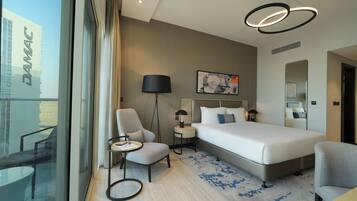 Una habitación de hotel moderna con una cama grande, un escritorio, una silla, una mesita, una lámpara y vistas a la ciudad a través de la ventana.