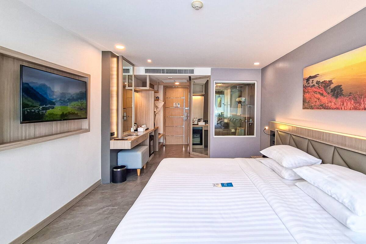 Hotelkamer met een groot bed, een badkamer met een douchecabine van glas, een televisie en een schilderij aan de muur.