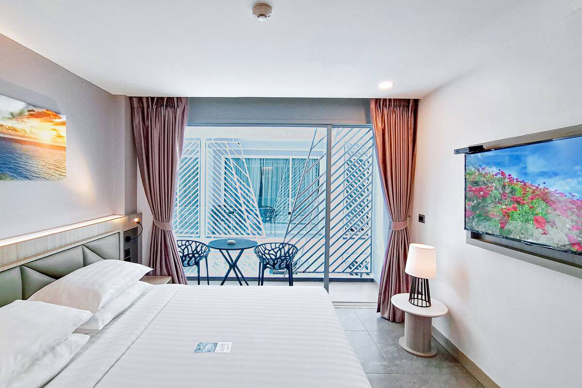 Een hotelkamer met een bed, een balkon met een tafel en stoelen, een schilderij aan de muur en een raam met gordijnen.