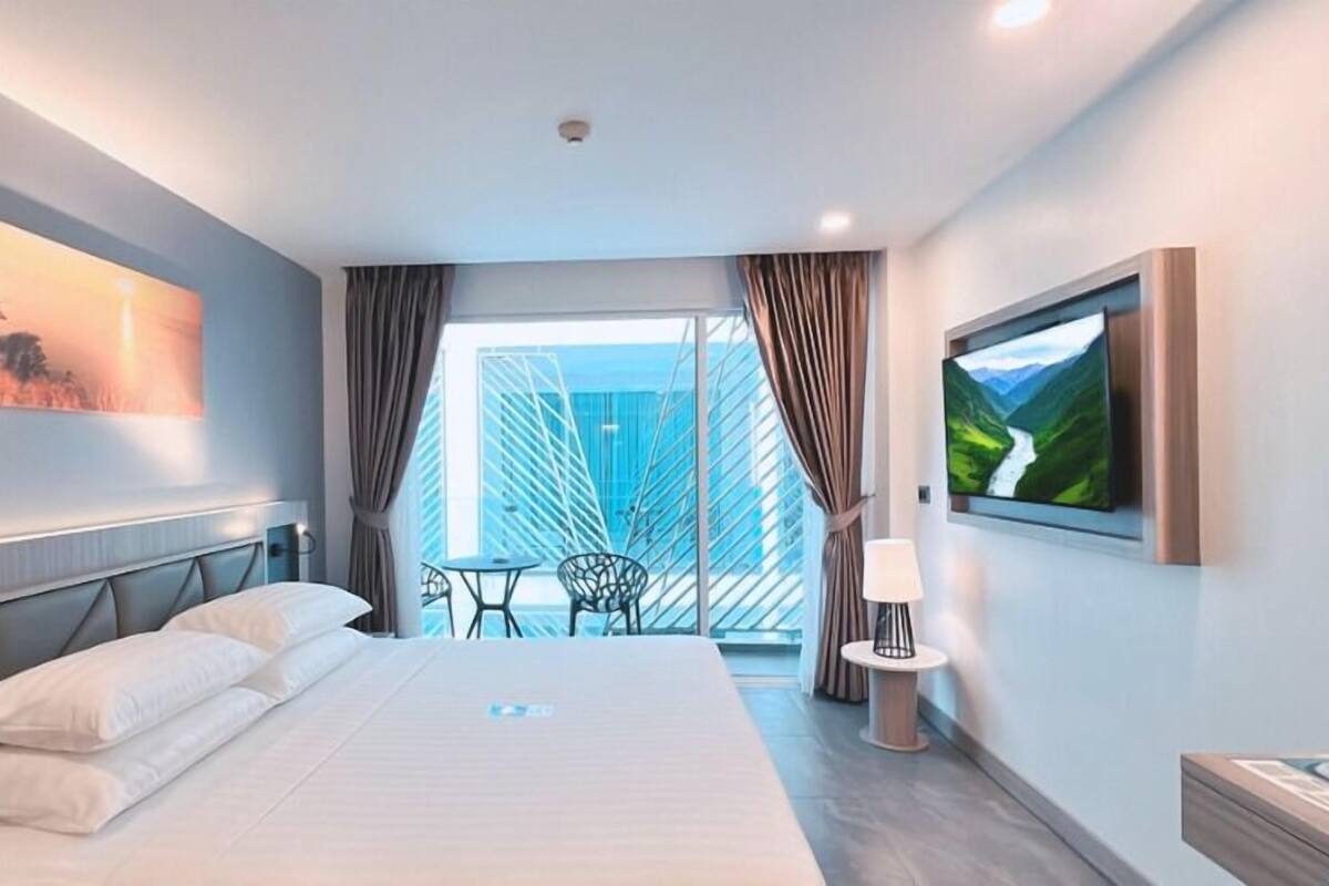 Een moderne hotelkamer met een groot bed, een balkon met uitzicht, een flatscreen-tv en een schilderij aan de muur.