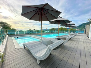 A poolside area with lounge chairs and umbrellas, a swimming pool, and a view of the mountains. - Clarian Hotel Beach Patong (Patong)