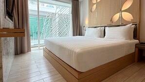A modern hotel room with a large bed, wooden headboard, and a balcony with a view. - Clarian Hotel Beach Patong (Patong)