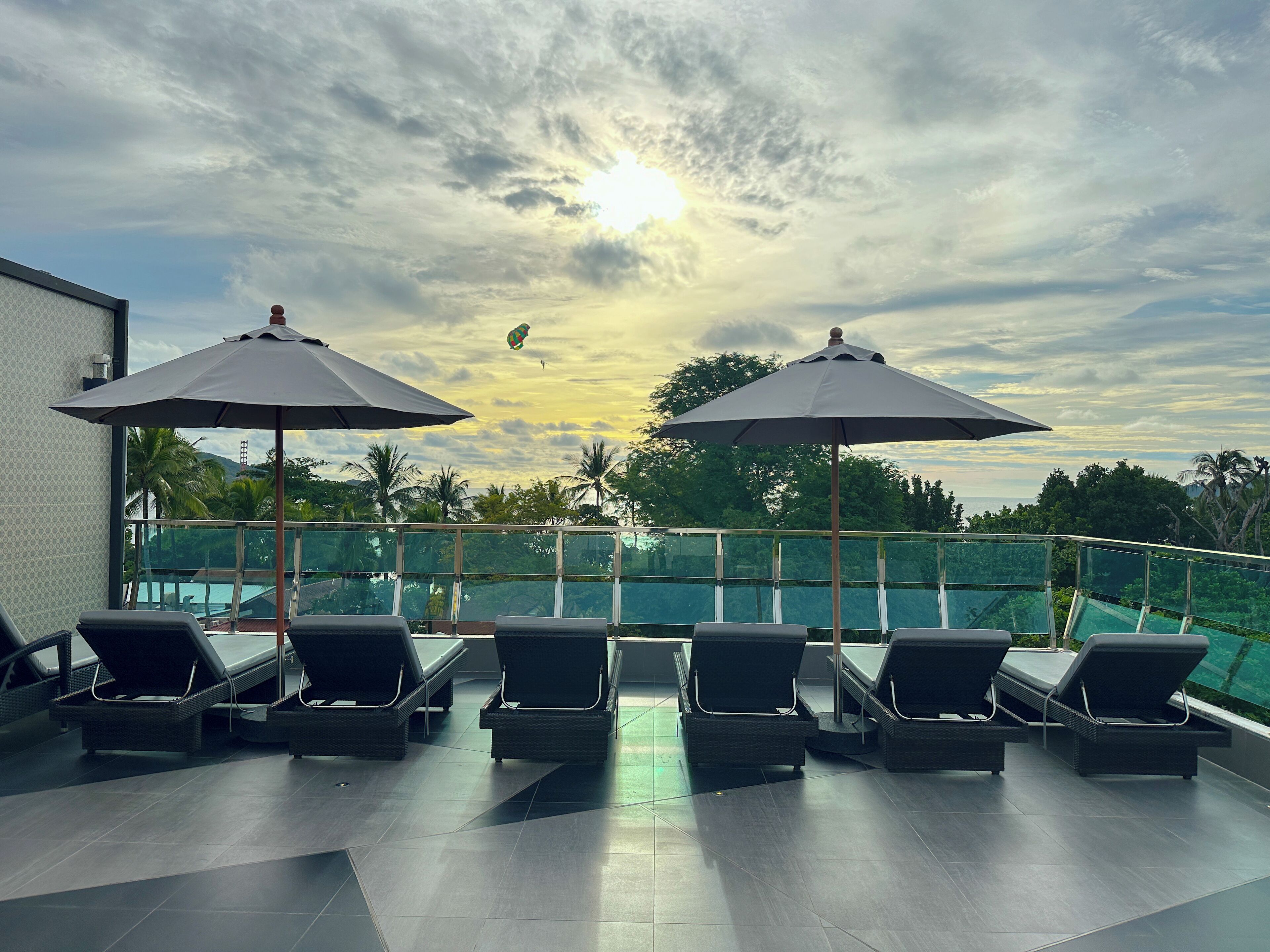 Eine Dachterrasse mit Liegestühlen und Sonnenschirmen, mit Blick auf einen Swimmingpool und üppiges Grün.