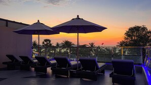 A rooftop terrace with lounge chairs and umbrellas, overlooking a sunset. - Clarian Hotel Beach Patong (Patong)