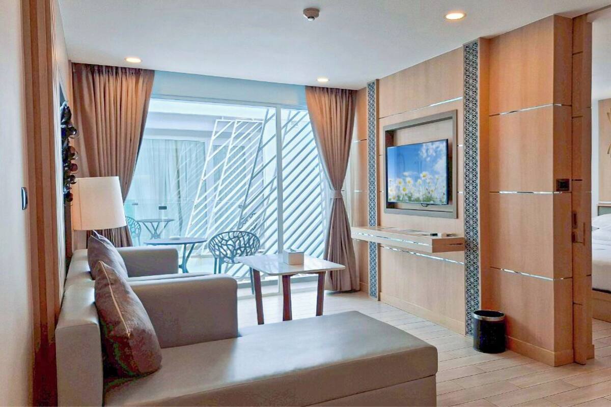 Een moderne hotelkamer met een bank, een klein tafeltje, een aan de muur bevestigde televisie, een bed met hoofdeinde en een groot raam met gordijnen.