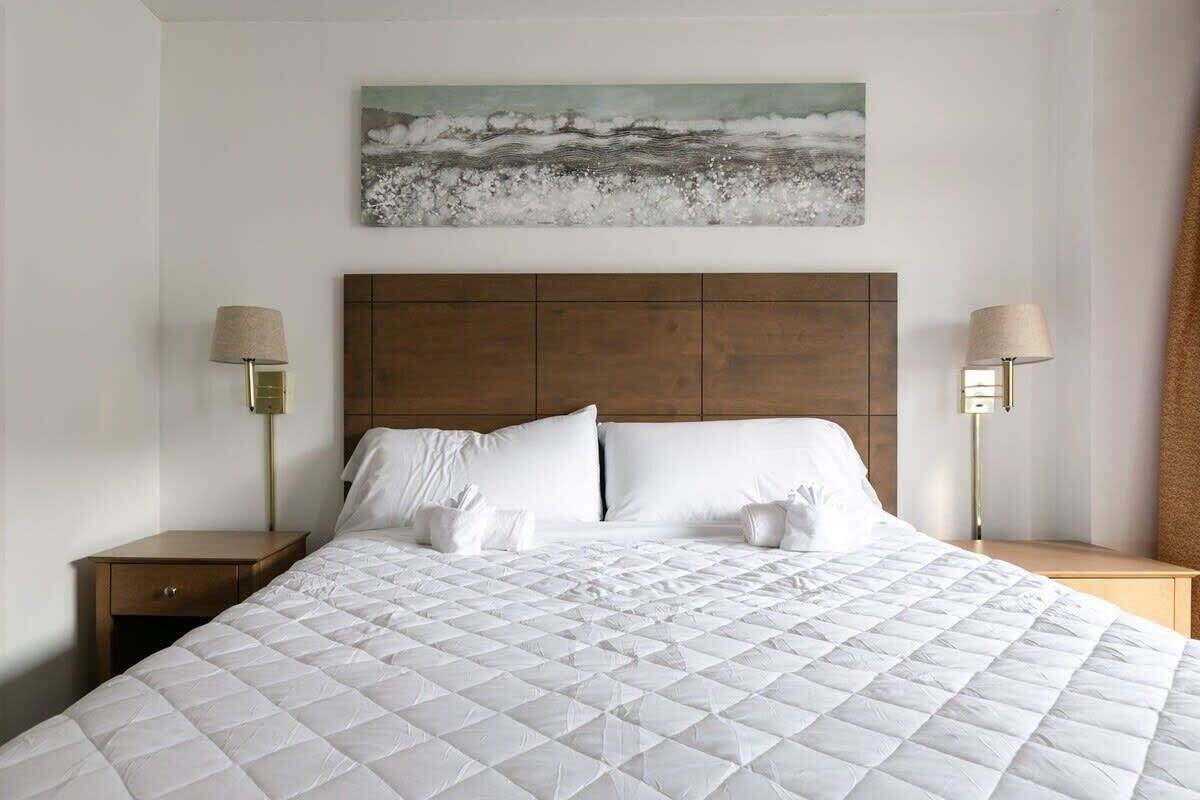 Ein Hotelzimmer mit einem großen Bett, zwei Nachttischlampen, einem Holzkopfstück und einem Gemälde von Wellen an der Wand.