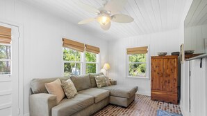 Ein gemütliches Zimmer mit einer Eckcouch, einem Holzkasten und einem Deckenventilator.