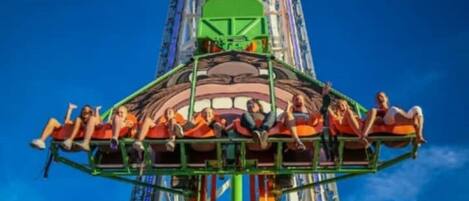 A ride with passengers seated in a circular arrangement, attached to a central structure with a green and orange color scheme.