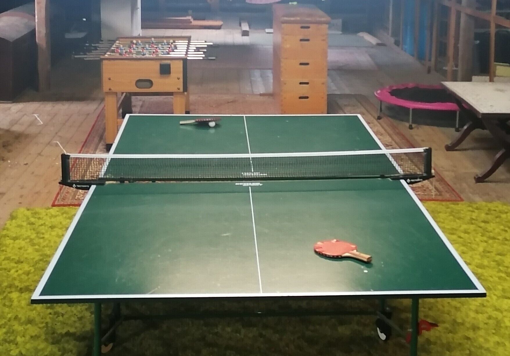 Een tafeltennistafel met een net in het midden, omringd door een groen vloerkleed.