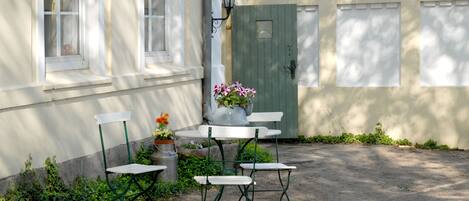 En innergård med ett bord och stolar, en krukväxt och en grön dörr.