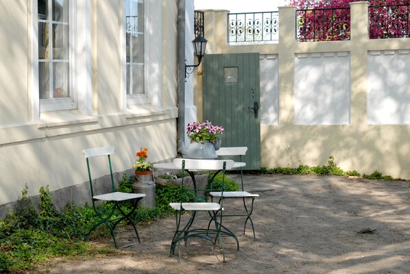 A courtyard with a table and chairs, a potted plant, and a green door.