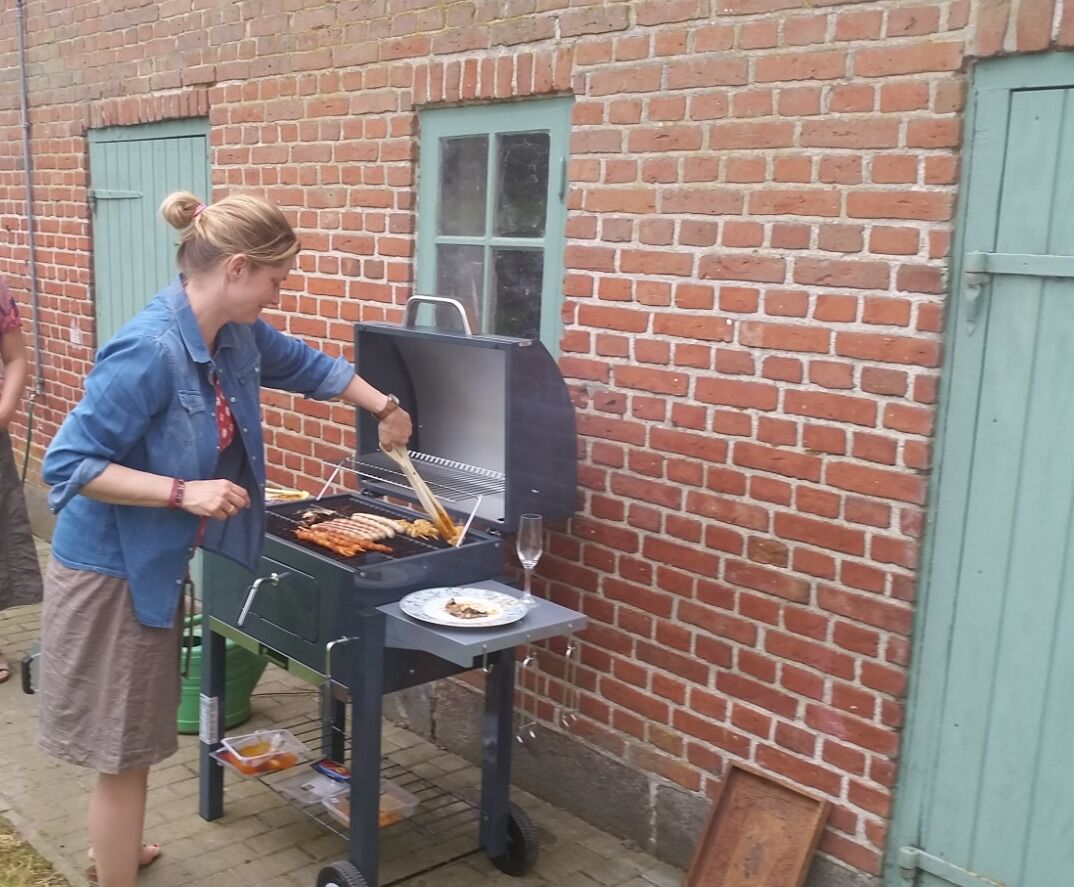 A person grilling food outdoors near a brick building with a green door.