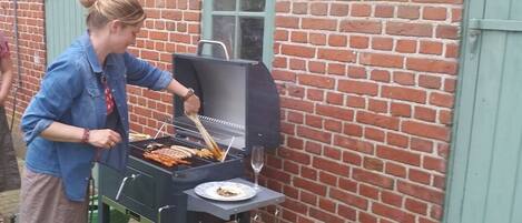 A person grilling food outdoors near a brick building with a green door.