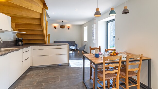 Eine moderne Küche mit einer Holztreppe, weißen Schränken und einem Essbereich mit einem Holztisch und Stühlen.