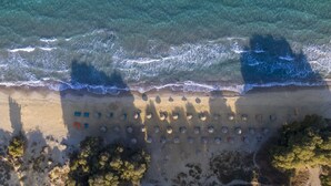 An aerial view of a beach with rows of umbrellas and beach chairs, a sandy shoreline, and waves approaching the shore. - Akti Coast Club (Kos)
