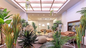 A spacious indoor area with a high ceiling, wooden flooring, and a variety of seating arrangements including sofas and chairs. - Akti Coast Club (Kos)