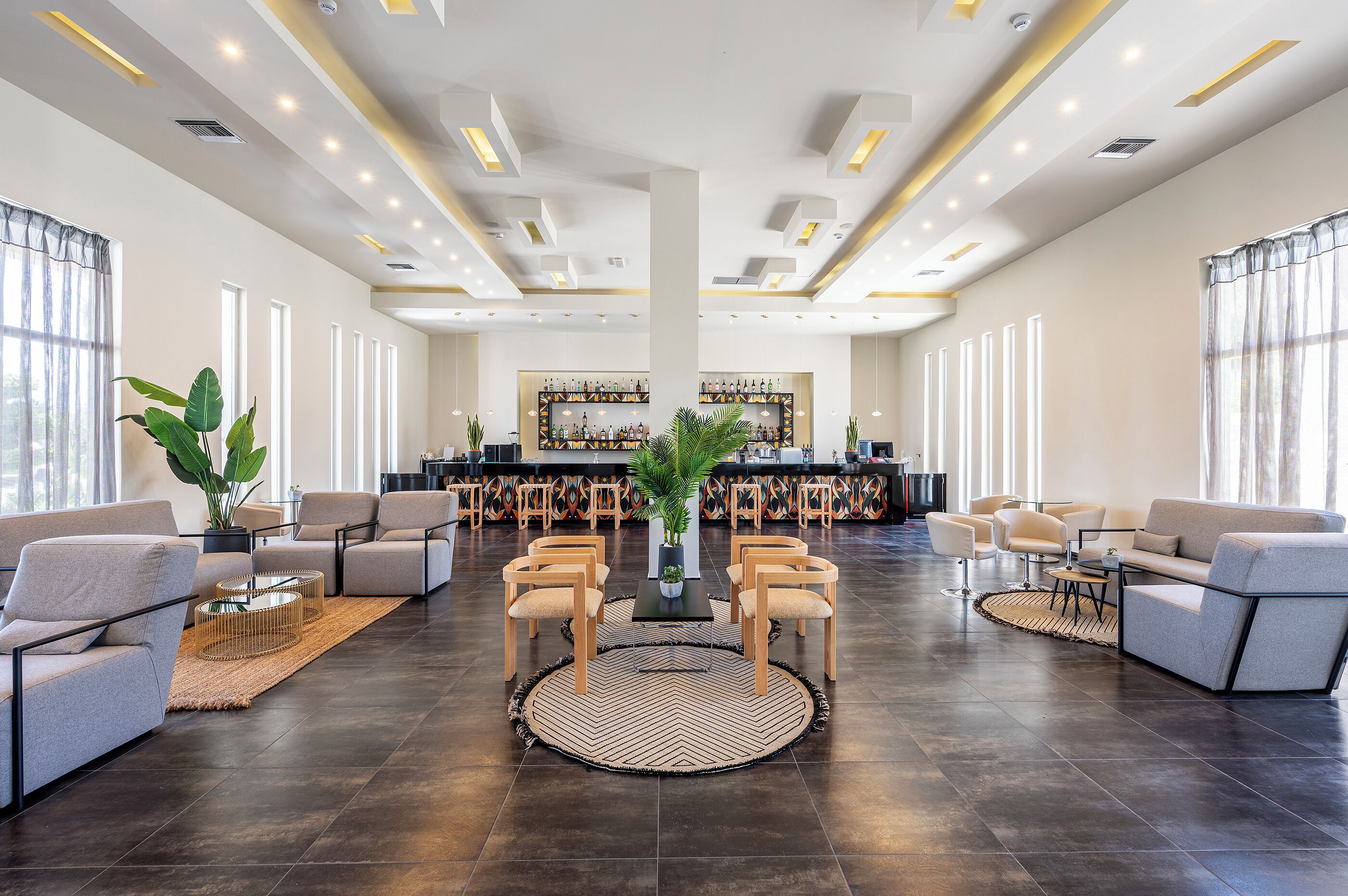 Eine großzügige Lobby mit einer zentralen Sitzecke, einer Bar im Hintergrund und großen Fenstern, die natürliches Licht hereinlassen.
