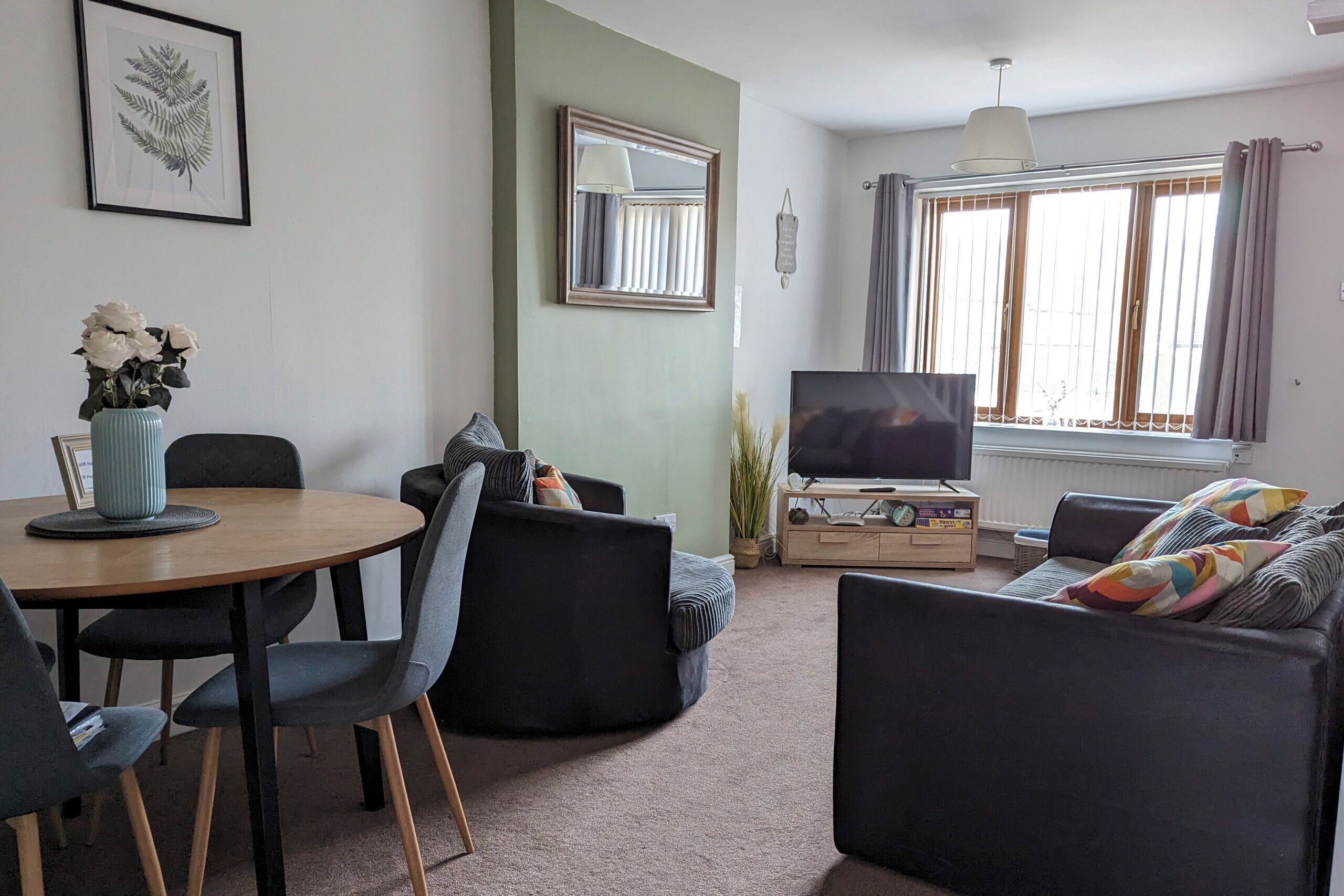 A living room with a round table, two sofas, a TV, and a window with curtains.