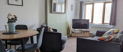 A living room with a round table, two sofas, a TV, and a window with curtains.