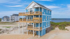 Una casa de playa de varios pisos con balcones, una playa de arena y vista al océano.