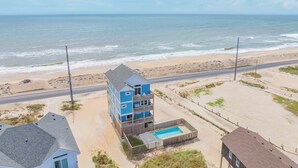Una propiedad frente a la playa con un edificio de dos pisos, una piscina y una carretera paralela a la costa.
