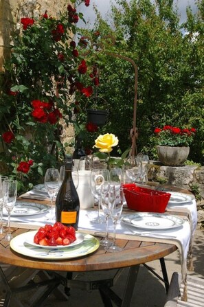An outdoor dining table set with plates, glasses, and a bottle, surrounded by lush greenery and flowers. - Manor Rectory16th,5*Heated pool, Air Cdg,1ha Park, Not overlooked,10mnDord Valey (NADAILLAC-DE-ROUGE)