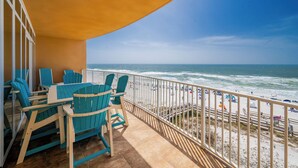 A balcony with a view of the ocean and beach, featuring a table and chairs.
