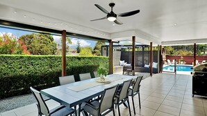 Une vaste terrasse dotée d’une table et de chaises, d’un ventilateur de plafond et offrant une vue sur une piscine.