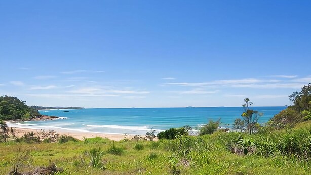 Un paysage côtier avec une plage, un ciel bleu clair et une végétation luxuriante.