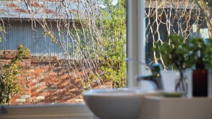 A view through a window with a brick wall, a metal roof, and a potted plant.