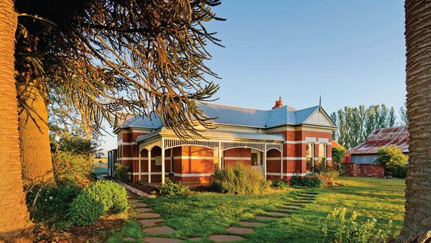 A brick building with a covered porch and a garden pathway leading to it.