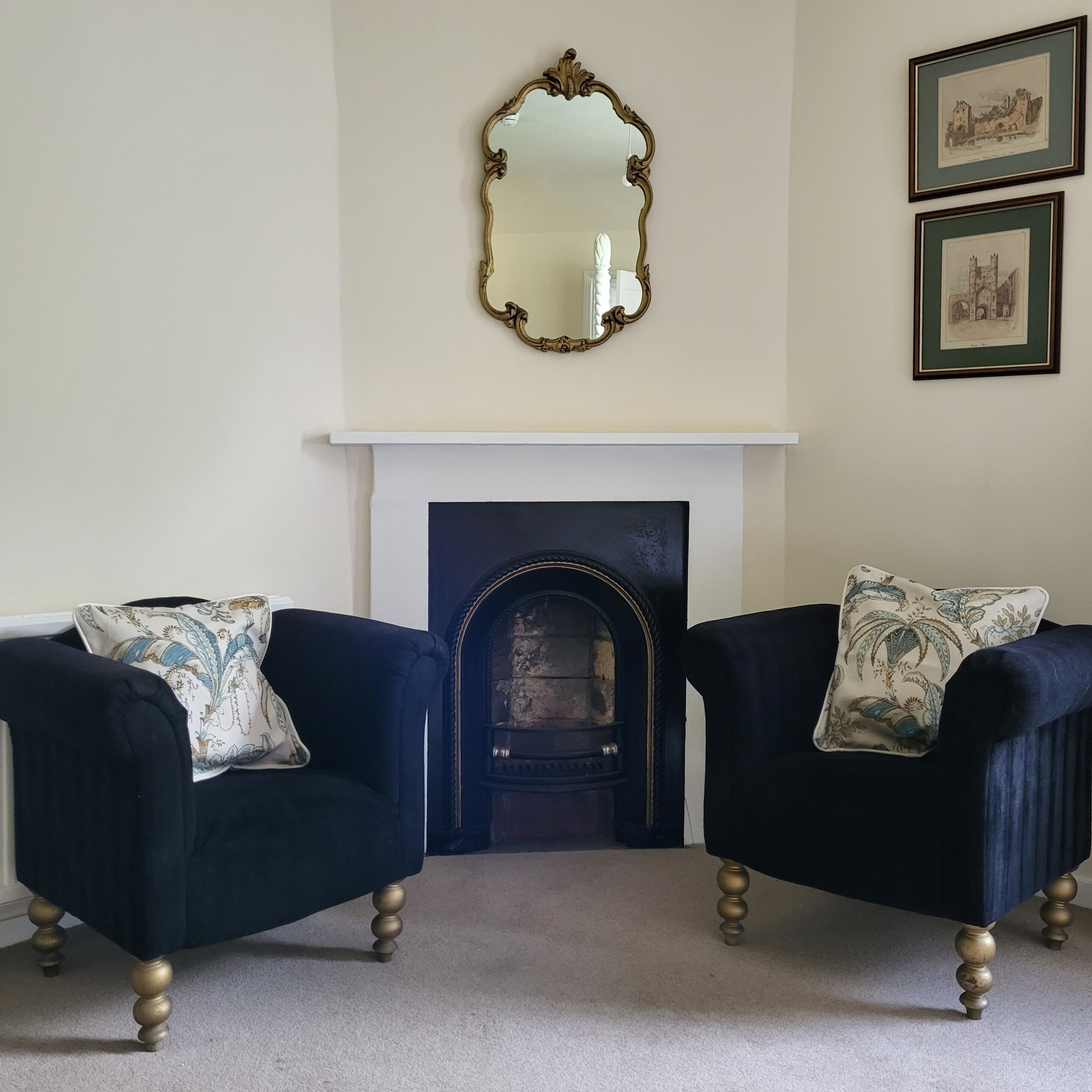 A room with two armchairs, a fireplace, a mirror, and framed pictures on the wall.