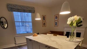 Een keuken met een marmeren aanrechtblad, houten kastjes, een groot raam en een hanglamp.