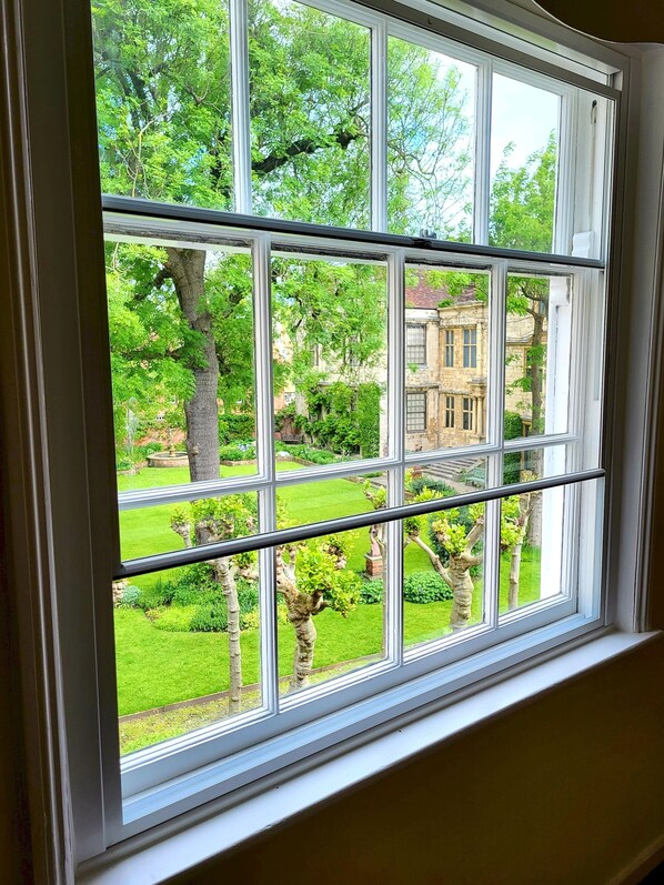 Ein Fenster mit Blick auf einen gepflegten Garten und ein historisches Gebäude.