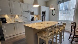 Een moderne keuken met een marmeren aanrechtblad, witte kasten en een centraal eiland met zitplaatsen.