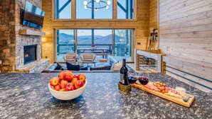 Ein gemütliches Blockhaus-Interieur mit Kamin aus Naturstein, einer Holzeinrichtung und einem großen Fenster mit Blick auf eine gebirgige Landschaft.