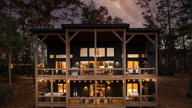 Eine zweistöckige Holzhütte mit mehreren Balkonen, großen Fenstern und Lichterketten.