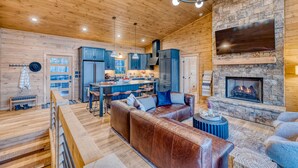 Ein gemütliches Blockhaus-Interieur mit Holzbalkendecke, Kamin aus Stein, einer Ledersofa und einer Küchenzeile.