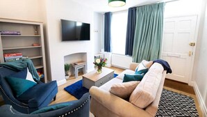 A living room with a sofa, armchair, coffee table, and a flat-screen TV mounted on the wall.