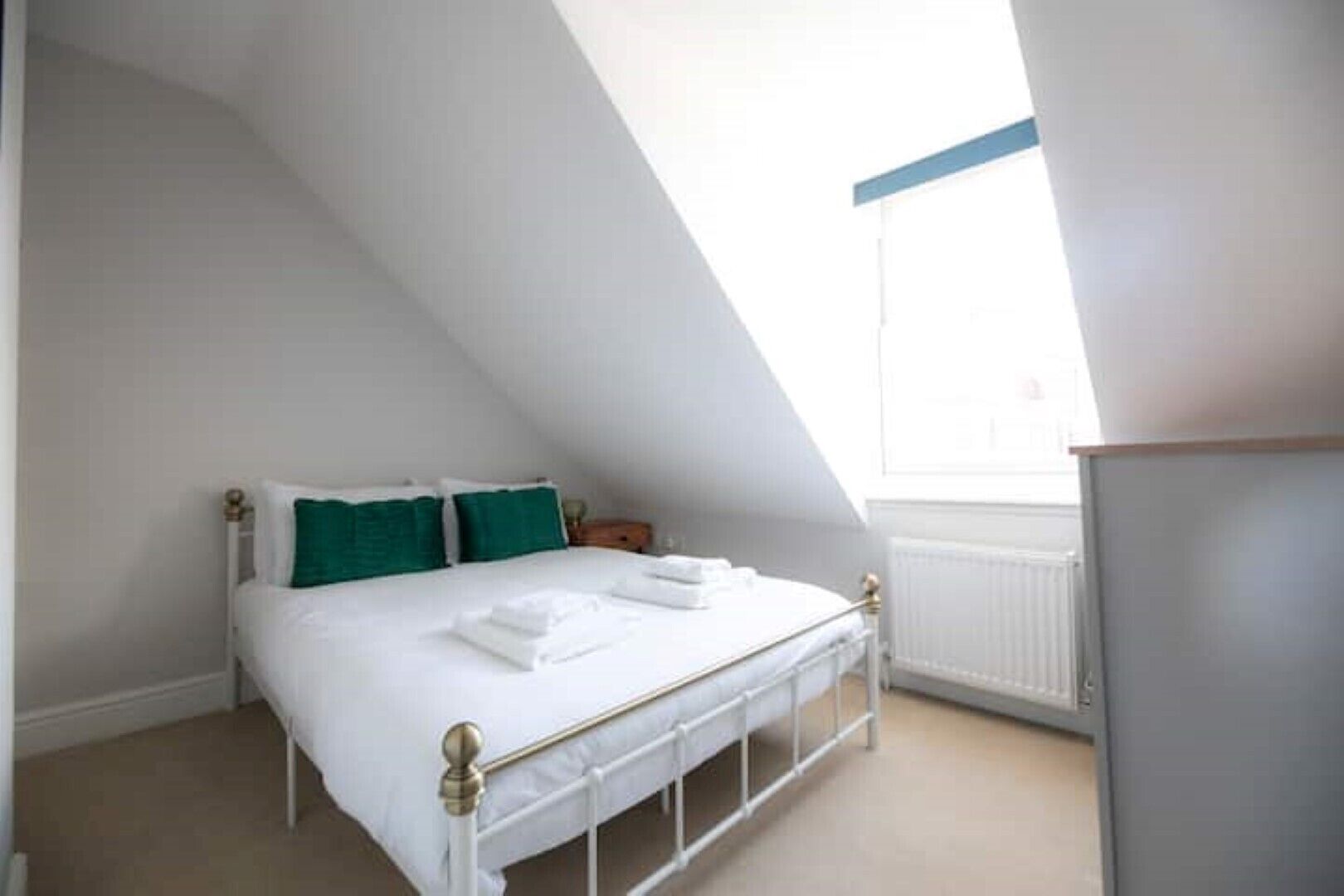 A bedroom with a white bed, green pillows, and a window with a blue frame.