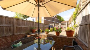 A patio with a table and chairs under a large umbrella, surrounded by brick walls and wooden fences.