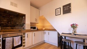 A modern kitchen with white cabinets, a stone backsplash, a microwave, and a small dining area with stools.