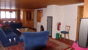 A room with a wooden ceiling, a dining table with blue chairs, a television, and a fire extinguisher. - Vacation apartment 1, Haus Gabi Vacation with pets (Bad Hindelang)