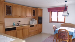 A kitchen with wooden cabinets, a dining table with chairs, and a window with curtains. - Vacation apartment 1, Haus Gabi Vacation with pets (Bad Hindelang)