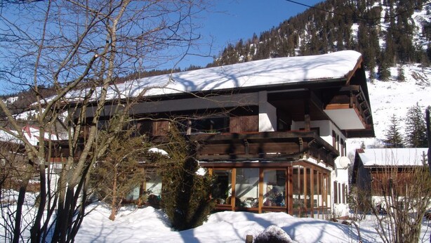 Un edificio de estilo chalé con un amplio ventanal, revestimiento de madera y tejado cubierto de nieve.