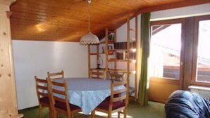Un comedor con una mesa redonda, sillas de madera, mantel azul y una lámpara colgante.