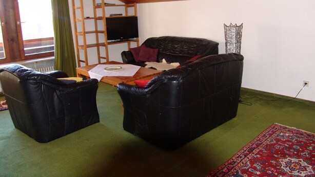 Una sala de estar acogedora con techo de madera, dos sofás de cuero negro, un televisor y una alfombra estampada.