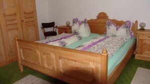 Una cama de madera con cabecera, una silla, una mesita de noche y un armario en una habitación con alfombra verde.